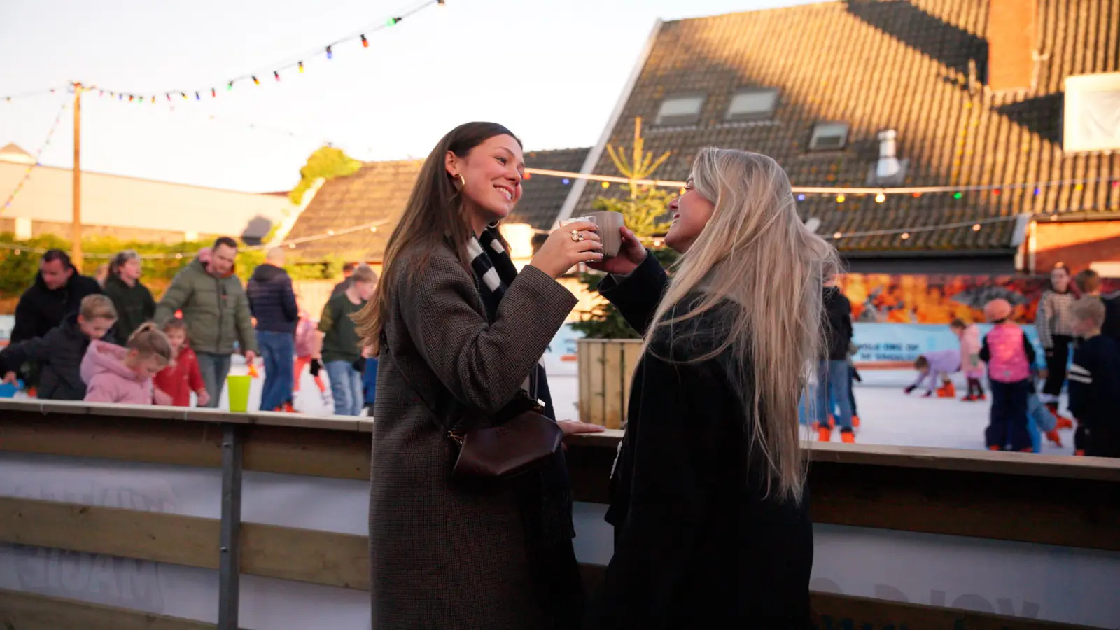 Twee bezoekers proosten met een beker warme chocomel langs de baan