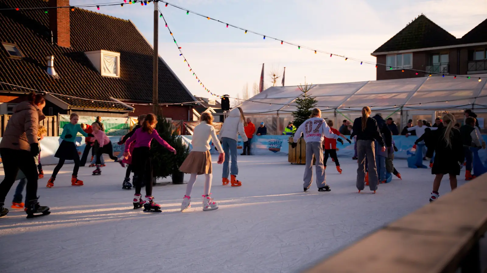Volle ijsbaan met schaatsers en lichtjes bij zonsondergang